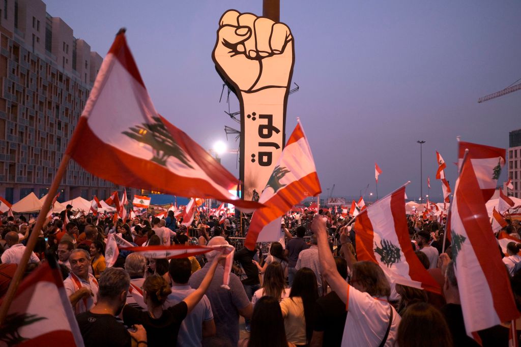 This picture taken on November 10, 2019 shows protesters waving Lebanese national flags by a giant sign of a fist with the slogan "revolution" written on it in Arabic in the capital Beirut's Martyrs' Square during continuing anti-government protests.
