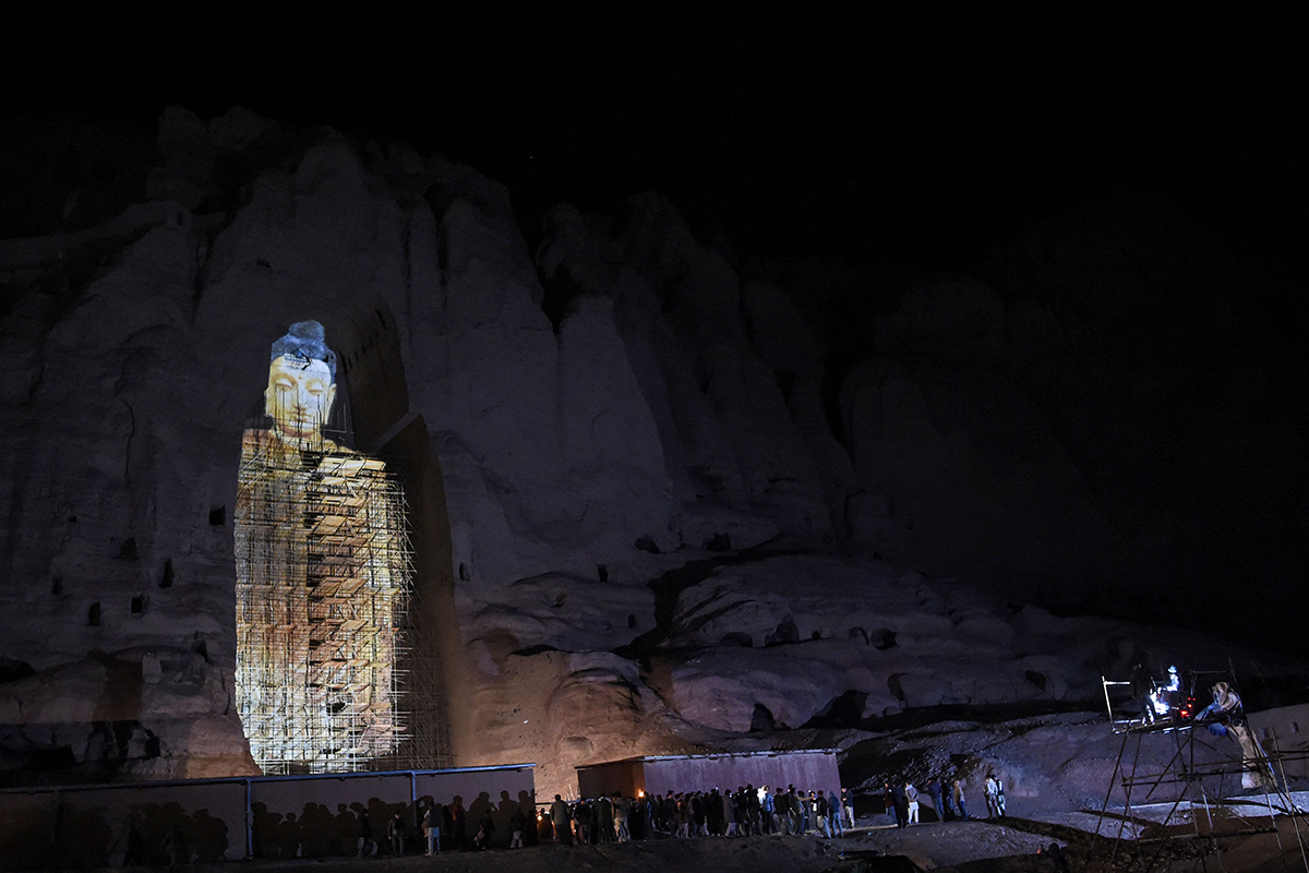 People watch a 3D projection of the 56-meter-high Salsal Buddha at the site where the Buddhas of Bamiyan stood before being destroyed by the Taliban in March 2001, on March 9, 2021. Photo by WAKIL KOHSAR/AFP via Getty Images.