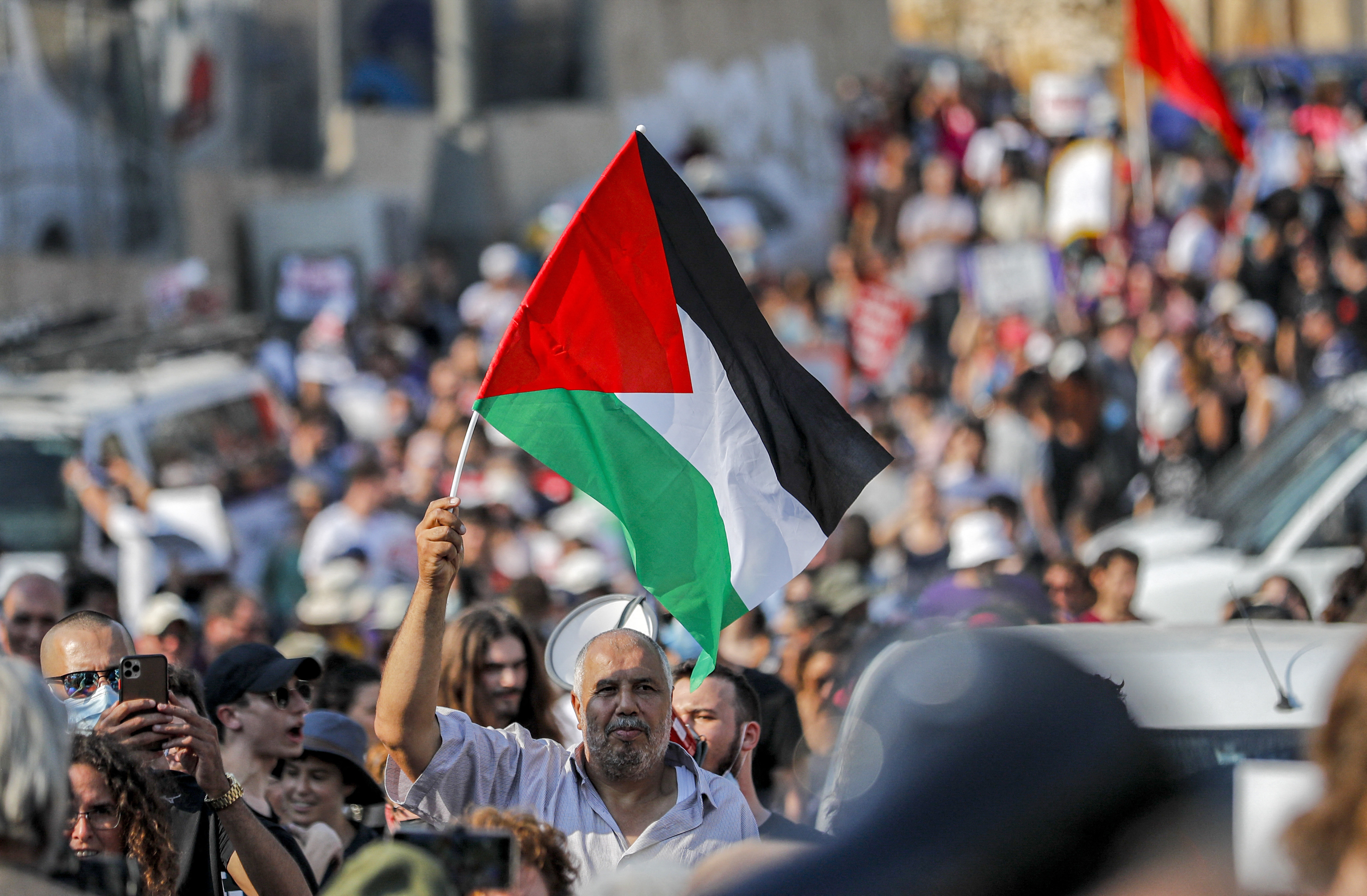 Photo above: A demonstrator raises a Palestinian flag during a demonstration by Palestinian, Israeli, and foreign activists against Israeli occupation and settlement activity in the Palestinian Territories and east Jerusalem in the Palestinian neighborhood of Sheikh Jarrah on July 30, 2021. Photo by AHMAD GHARABLI/AFP via Getty Images.