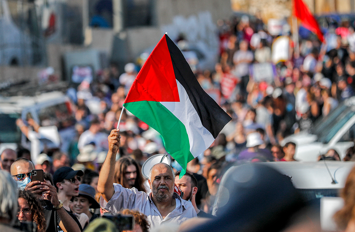 A demonstrator raises a Palestinian flag during a demonstration by Palestinian, Israeli, and foreign activists against Israeli occupation and settlement activity in Jerusalem’s Sheikh Jarrah neighborhood on July 30, 2021. Photo by AHMAD GHARABLI/AFP via Getty Images.