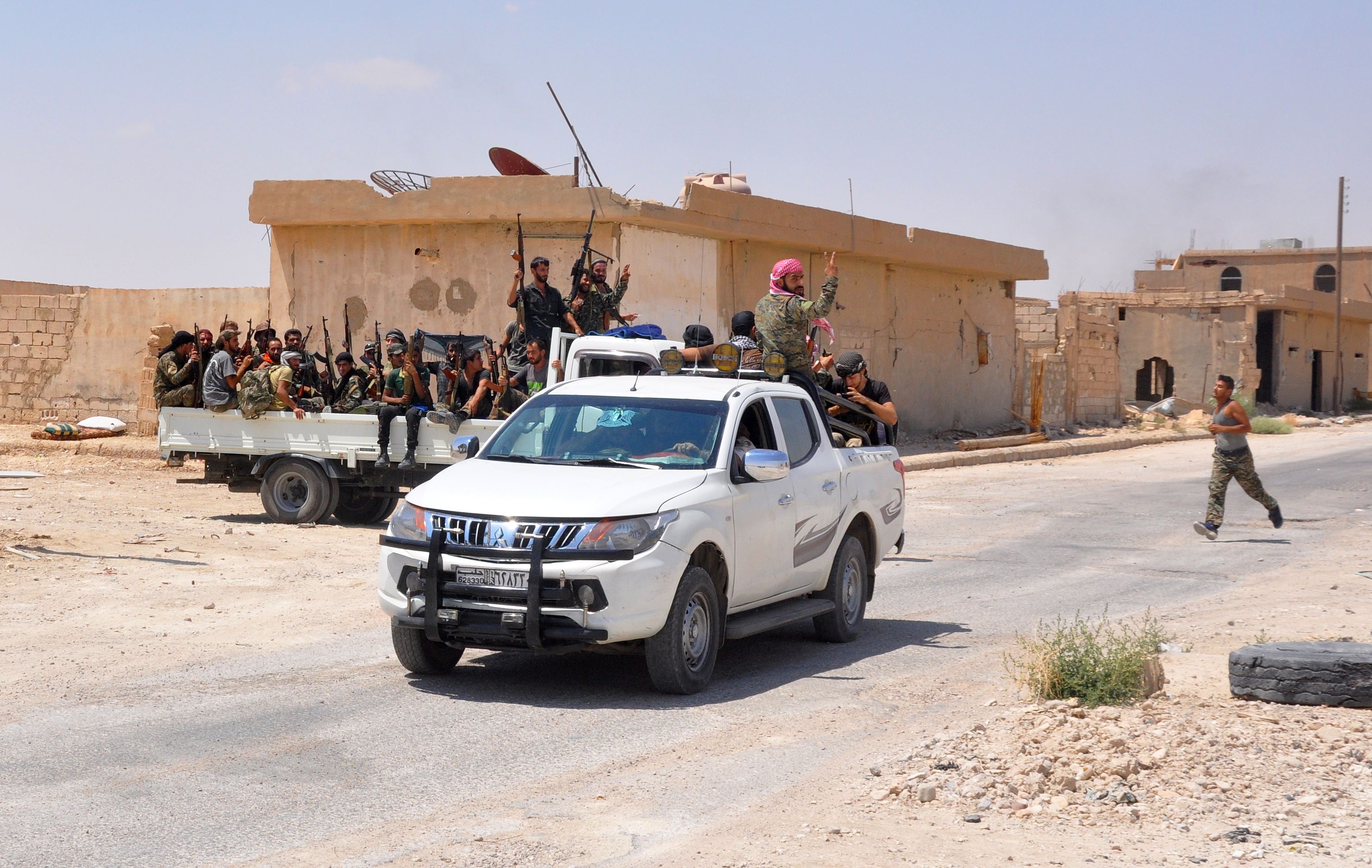 Photo above: Pro-government fighters sit in the back of vehicles brandishing their weapons and flashing the sign for victory in the central Syrian town of al-Sukhnah, situated in the county’s large desert area called the Badia, on August 13, 2017 as they clear the area after taking control of the city from Islamic State group fighters. Photo by STRINGER/AFP via Getty Images.