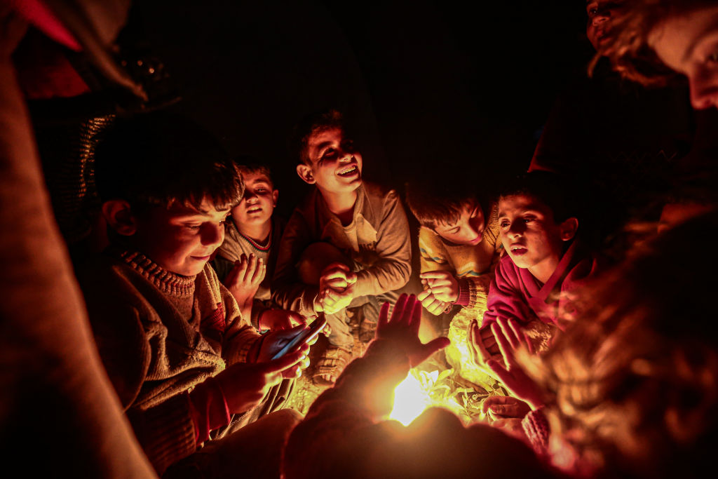 Syrian kids are seen warming around a fire they burn in the evening, on March 06, 2020 in Idlib, Syria. Civilians, who have been fled due to the ongoing attacks in the Idlib de-escalation zone in Syria carried out by Assad regime, Russia and Iranian-backed terrorist groups, and reached Turkish border, struggling to live under hard conditions at Maâarrat Misrin refugee camp. (Photo by Muhammed Said/Anadolu Agency via Getty Images)