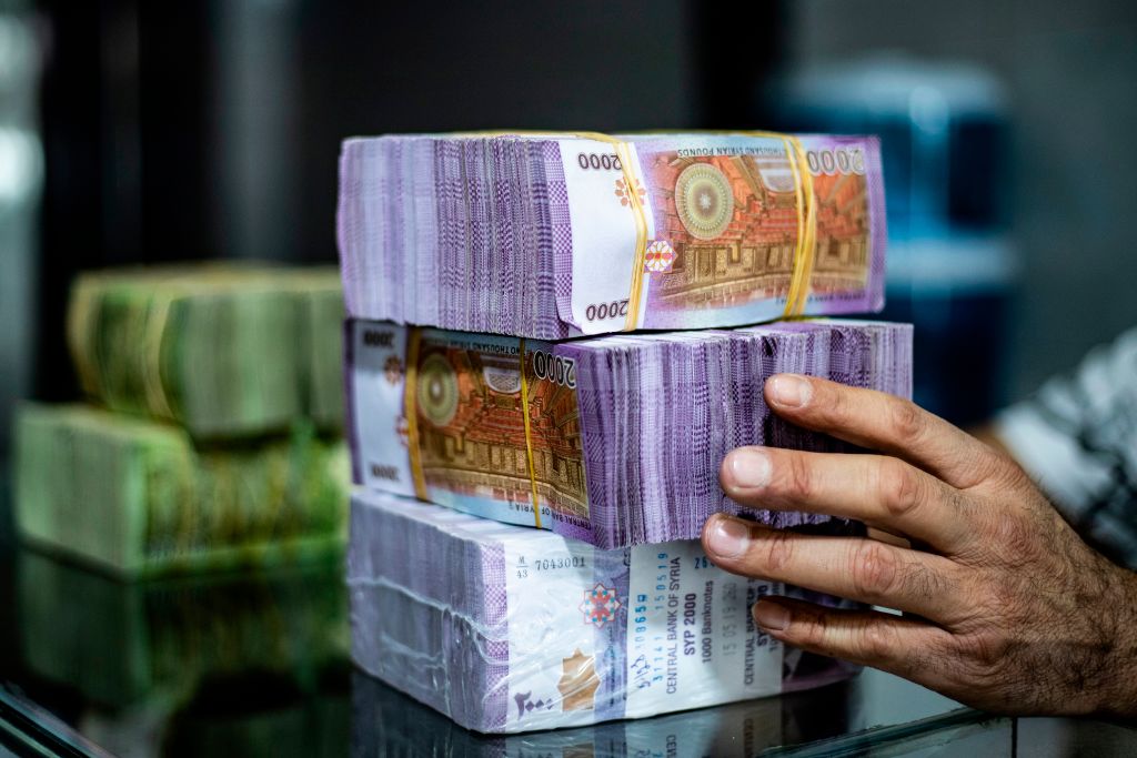 A merchant arranges stacks of Syrian pounds at a market in the Kurdish-majority city of Qamishli in northeast Syria on September 10, 2019. - The declining value of the pound is a sure sign of Syria's ailing economy. The civil war has battered the country's finances and depleted its foreign reserves. A flurry of international sanctions on President Bashar al-Assad's regime and associated businessmen since the start of the war in 2011 has compounded the situation. (Photo by Delil SOULEIMAN / AFP) (Photo credit should read DELIL SOULEIMAN/AFP via Getty Images)
