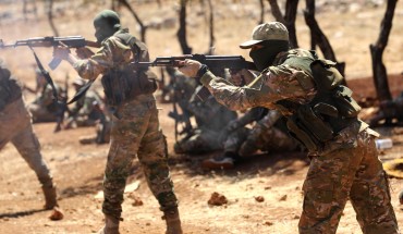 Syrian fighters fire AK-47 at a mock battle during a graduation of new Hayat Tahrir al-Sham (HTS) members