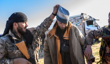 A member of the SDF raises the hood of a Bosnian man suspected of being an ISIS fighter as he is searched after leaving the group’s last holdout of Baghouz, on March 1, 2019.