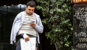 A man looks at a smartphone in his hand while walking outside along a street in the Iranian capital Tehran on November 17, 2019. - Iran's supreme leader on November 17 threw his support behind a decision to hike petrol prices, a move that sparked nationwide unrest in which he said "some lost their lives". Access to the internet has been restricted since demonstrations broke out two days prior, after a decision by the Supreme National Security Council of Iran.