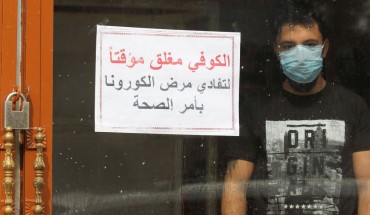 An Iraqi man, wearing a protective mask, stands inside a coffee shop with a sign in Arabic which reads "Coffee shop is closed, due to corona following a decision by the Health ministry" in the capital Baghdad on March 16, 2020 amidst efforts against the spread of COVID-19 coronavirus disease. 