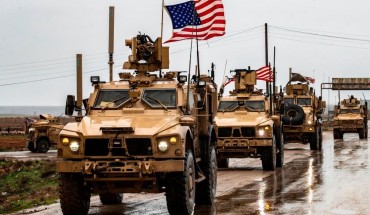 A row of U.S. troops with flags waving in Syria.