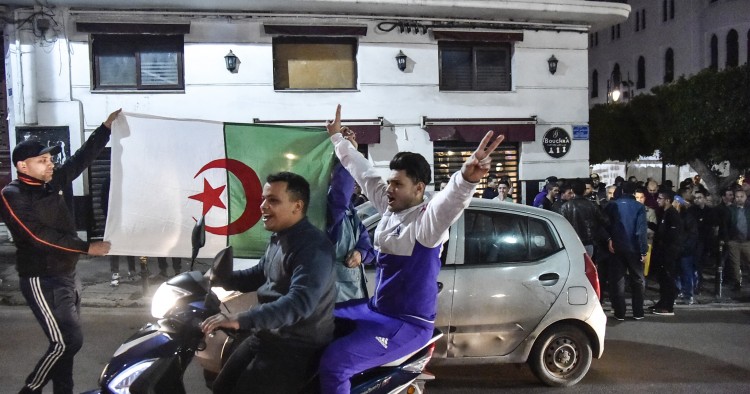 An Algerian flashes the victory gesture while seated on a scooter as another two hold a national flag behind him during a demonstration in the centre of the capital Algiers on March 11, 2019, after President Abdelaziz Bouteflika announced his withdrawal from a bid to win another term in office and postponed an April 18 election, following weeks of protests against his candidacy.