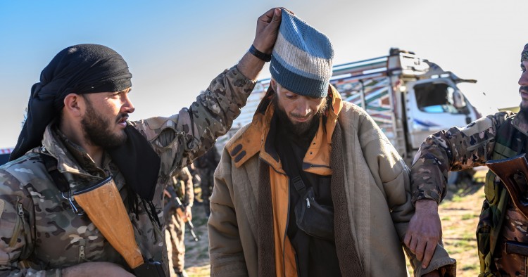 A member of the SDF raises the hood of a Bosnian man suspected of being an ISIS fighter as he is searched after leaving the group’s last holdout of Baghouz, on March 1, 2019.