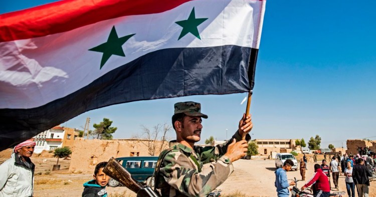  A Syrian regime soldier waves the national flag a street on the western entrance of the town of Tal Tamr in the countryside of Syria's northeastern Hasakeh province on October 14, 2019. 