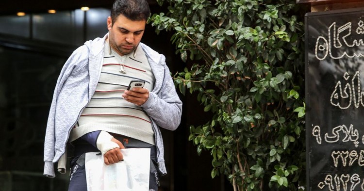 A man looks at a smartphone in his hand while walking outside along a street in the Iranian capital Tehran on November 17, 2019. - Iran's supreme leader on November 17 threw his support behind a decision to hike petrol prices, a move that sparked nationwide unrest in which he said "some lost their lives". Access to the internet has been restricted since demonstrations broke out two days prior, after a decision by the Supreme National Security Council of Iran.