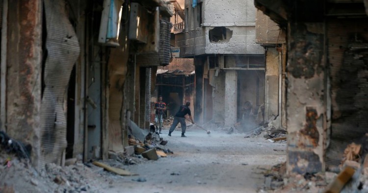 A man cleans in a street near destroyed buildings in the Palestinian camp of Yarmuk southern Damascus on November 1, 2018. - Former residents of the Palestinian camp of Yarmuk are desperately counting on help from abroad to help raise the once-bustling neighbourhood back out of the rubble.