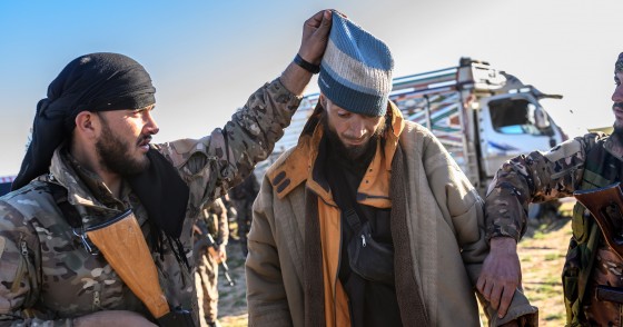 A member of the SDF raises the hood of a Bosnian man suspected of being an ISIS fighter as he is searched after leaving the group’s last holdout of Baghouz, on March 1, 2019.