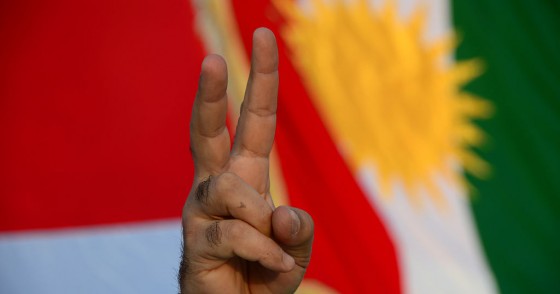 A demonstrator makes the "victory" sign standing in front of a Kurdish flag.