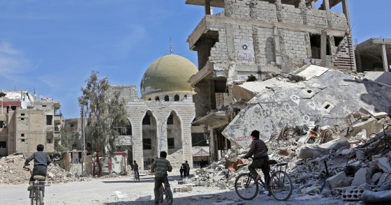 Syrian children ride their bike past destroyed buildings in the former rebel-held town of Zamalka, in Eastern Ghouta on April 5, 2018. / AFP PHOTO / STRINGER (Photo credit should read STRINGER/AFP via Getty Images)