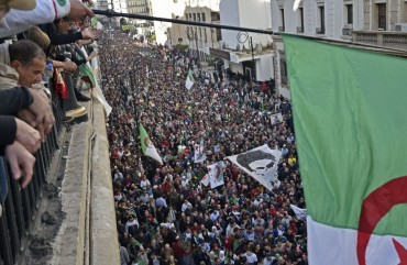 Algerians wave a national flag from a balcony as they watch anti-government demonstrators march in the capital Algiers on December 6, 2019, ahead of the presidential vote scheduled for December 12.
