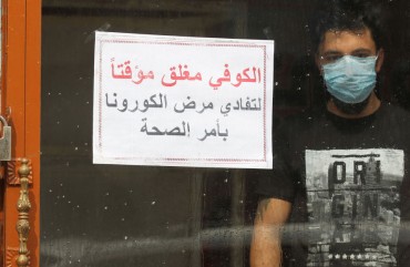 An Iraqi man, wearing a protective mask, stands inside a coffee shop with a sign in Arabic which reads "Coffee shop is closed, due to corona following a decision by the Health ministry" in the capital Baghdad on March 16, 2020 amidst efforts against the spread of COVID-19 coronavirus disease. 